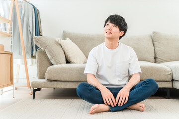 Fototapeta premium A smiling young Asian man sitting in front of the sofa in the living room.