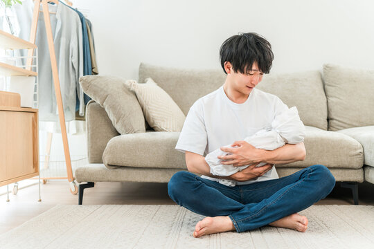 A young Asian man holding a baby in his living room.
