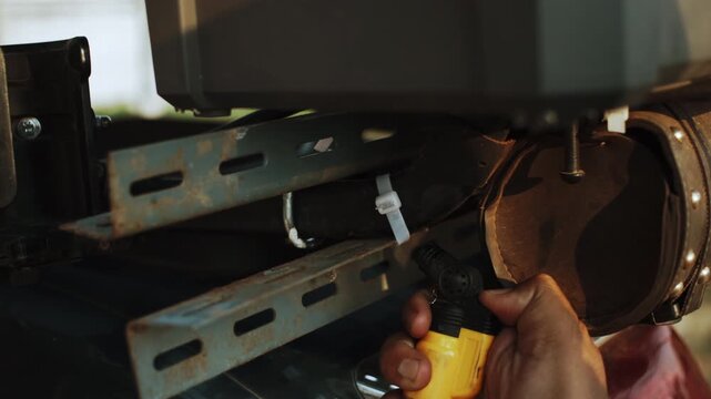 A man carefully uses a pocket lighter flame to burn through a white nylon zip tie on a black background.
