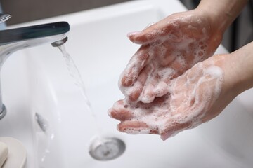 Fototapeta premium Woman washing hands with soap above white sink indoors, closeup