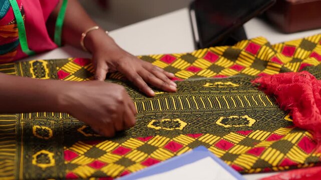 African tailor's hands marking colorful ankara fabric with chalk on a workspace