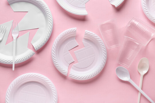 Plastic plates with cups and cutlery on pink background