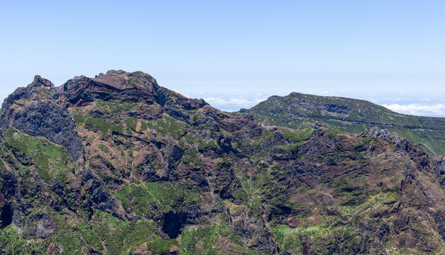Volcanic mountain peaks dominate Madeira's PR1 Vereda do Areeiro trail. Rugged cliffs frame the high-altitude hiking path. Dramatic clouds hover over scenic Portuguese landscapes.