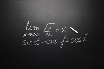 Obraz premium White chalk with written mathematical formulas on blackboard