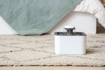Automatic pet water fountain on floor near bed in bedroom