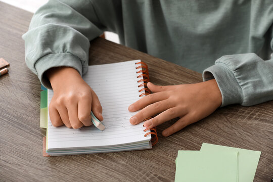 Child erasing mistake in notebook at table, closeup