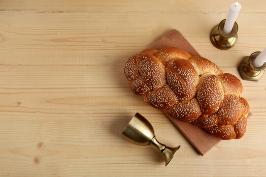 Traditional challah bread with wine goblet and burning candles on wooden table. Shabbat Shalom