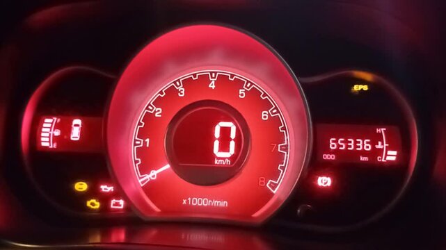 Close-up of a modern car dashboard with multiple warning lights illuminated, digital speedometer at zero, glowing red panel in a dark environment.