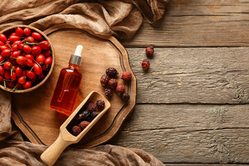 Bottle of cosmetic rose hip oil and bowl with berries on wooden background