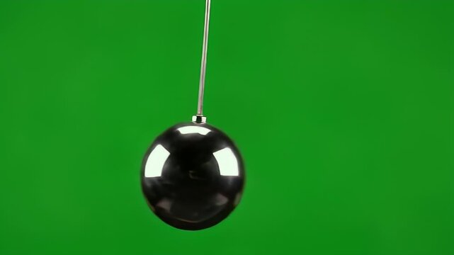 A polished, dark, egg-shaped object hangs from a thin wire against a green background