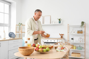 Fototapeta premium Mature man with honey making apple cider at table in kitchen