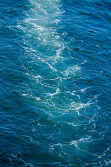 Fototapeta premium Strong white boat wake and foamy trail on the surface of deep blue ocean water under a bright sunny sky in a tropical resort.