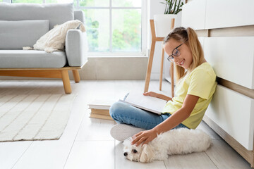 Fototapeta premium Cute little happy girl with Maltese dog reading book on floor near commode at home