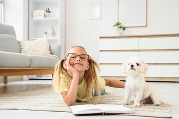 Fototapeta premium Cute little happy girl with Maltese dog reading book on floor at home