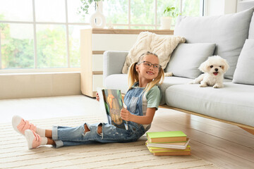 Fototapeta premium Cute little happy girl with Maltese dog and books reading on floor at home