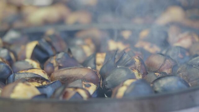 Close up of roasted chestnuts cooking in a large pan with smoke rising