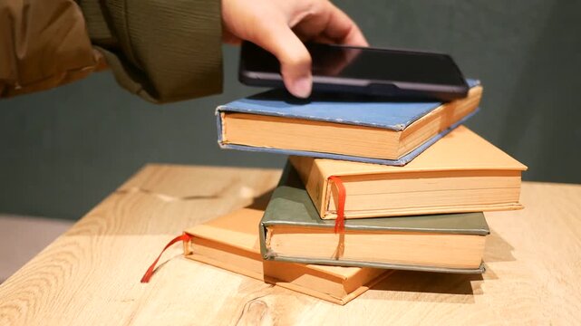 A hand picking up smartphone from stack of old books, showing education technology concept and digital literacy