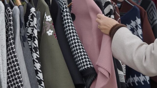 Woman hand browsing through stylish knitwear collection on clothes rack at outdoor market
