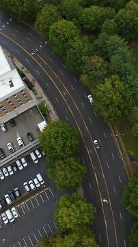 Vertical screen Aerial View Corporate Campus Curve Road With Adjacent Parking And Office Block, Mature Trees Lining Asphalt, Steady Commuter Traffic Passing Curved Lanes, Overcast Sky