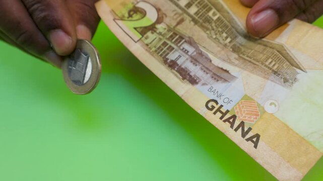 A close-up shot of hands displaying a 2 Ghanaian Cedi coin and banknote. The video highlights the currency's details, including Kwame Nkrumah's portrait, over a vivid green backdrop.