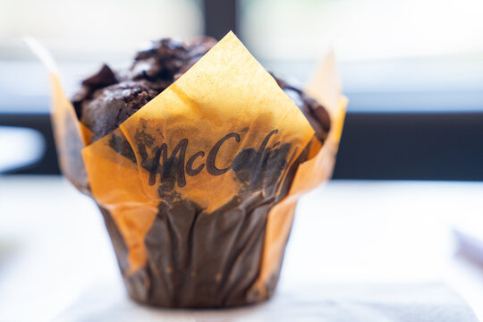 Belgrade, Serbia: July 3, 2024:Chocolate muffin in a brown and orange McCafe McDonalds paper wrapper table, soft background blur bright window light, single serving takeaway dessert snack close up