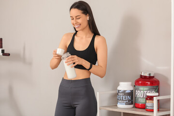 Fototapeta premium Sporty young happy woman making protein shake in gym