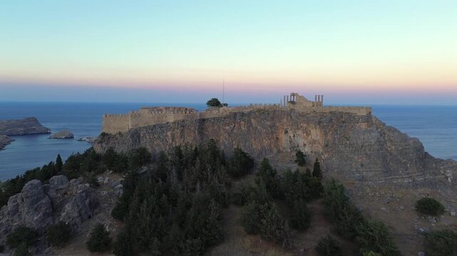 Cinematic drone panorama of the ancient Acropolis of Lindos during blue hour. Stunning high-angle view of the Temple of Athena Lindia, medieval walls, and the Aegean sea. Ideal for history and travel.
