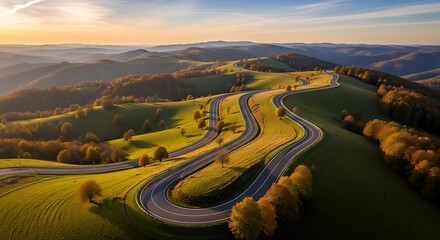 Fototapeta premium Winding road passes through rolling hills and trees during sunset