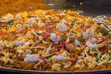 A vibrant close-up of Pad Thai stir-fried in a wok with shrimp, eggs, bean sprouts, and chives, showcasing the rich textures and colors of Thai street food. © VikSid