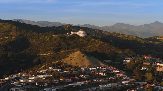 Los Angeles, California USA - FEBRUARY 25, 2026: Wide aerial shot of Griffith Observatory surrounded by hills and mountains at sunset with warm light and detailed city neighborhood below.