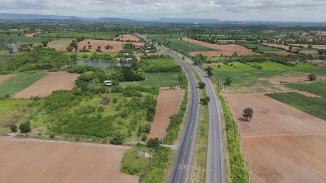 Drone aerial view of rural farmland with country road crossing agricultural fields. Countryside landscape showing agriculture