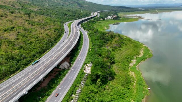 Aerial view of highway running along river and green hills. Transportation, infrastructure, travel and logistics concept