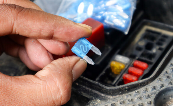 A close-up of a hand holding a blue automotive fuse, showing its transparent plastic casing and metal connectors, commonly used for circuit protection in vehicles.