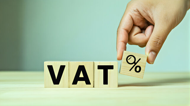 Wooden blocks spelling VAT with a hand placing a percentage symbol block, representing value-added tax