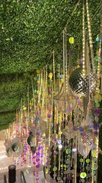 4k video of Hanging silver reflective and shimmering decoration with baubles and tassels, with green vertical garden ceiling, hanging plants from above. Festive organic natural decoration. 