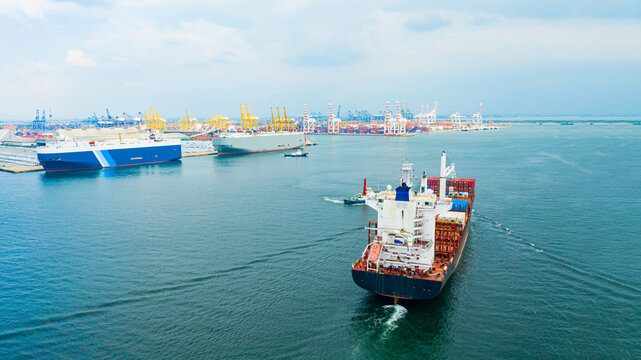 multiple cargo vessels navigating across calm blue water near busy container port, with cranes, dock facilities, and industrial harbor stretching into distance, symbolizing global trade,  