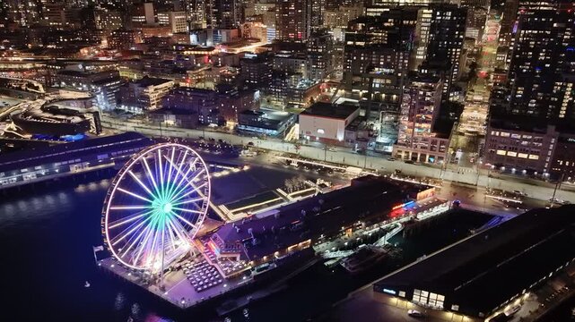 Seattle downtown skyline and waterfront with illuminated ferris wheel reflecting on Elliott Bay at night aerial view. g.
