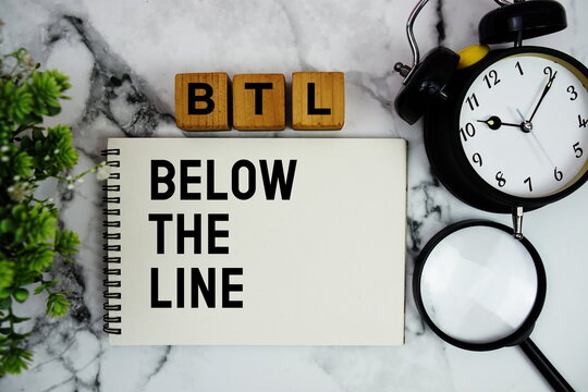 BTL Below The Line text with alarm clock and magnifying glass on marble background
