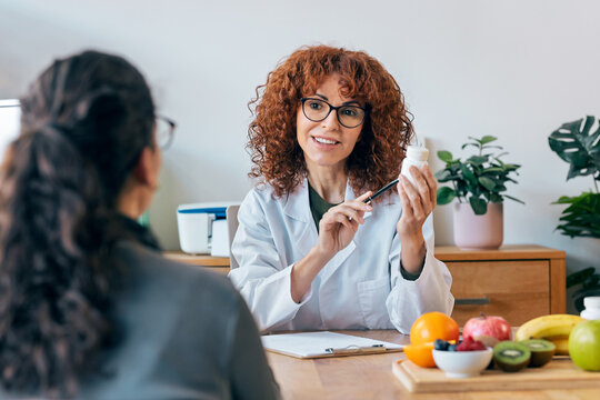 Beautiful cheerful female nutritionist talking while explaining medical treatment to patient in the consultation.