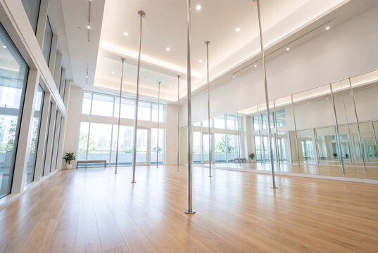 Modern empty pole dance studio interior with wooden floors, large mirrors and polished metal poles