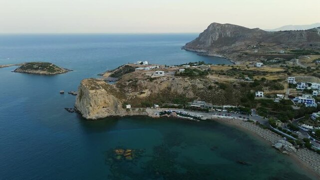 Cinematic high-angle drone shot of Stegna Beach in Rhodes. Stunning panoramic view of turquoise waters, traditional white buildings, and dramatic rocky formations. Ideal for travel storytelling