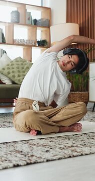 Fitness, stretching and tablet with yoga man in home living room for balance or flexibility. App, headphones and streaming with Asian person on floor in apartment for exercise or wellness activity