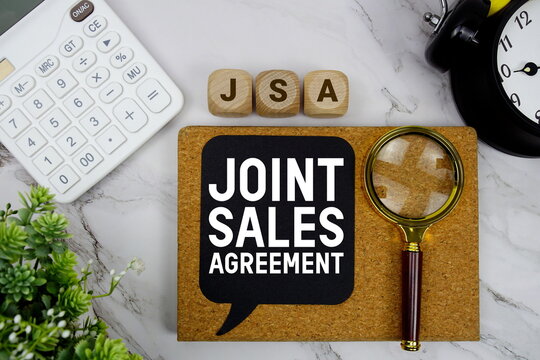 JSA Joint Sales Agreement text with calculator, magnifying glass and alarm clock on marble background