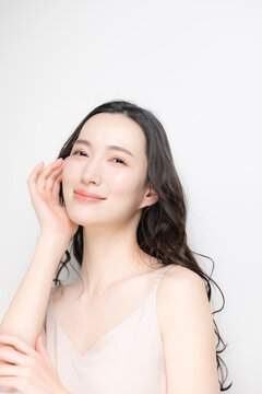黒髪のパーマのロングヘアで白背景の若い女性のビューティーイメージ　スキンケアなどのツヤ肌、透明感がある保湿や高級感のあるラグジュアリーな美容イメージカメラ目線