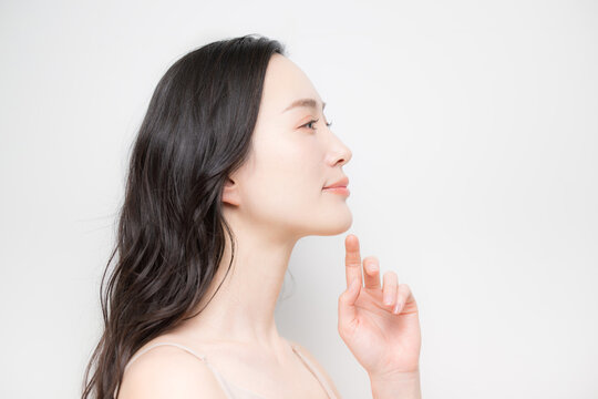 黒髪のパーマのロングヘアで白背景の若い女性のビューティーイメージ　スキンケアなどのツヤ肌、透明感がある保湿や高級感のあるラグジュアリーな美容イメージの美しいeラインの横顔
