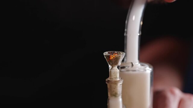 Close up of cannabis bowl burning in glass bong with smoke rising.
