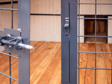 Close-up of kennel door latch and metal mesh in dog enclosure, symbolizing security, control and potential escape, with blurred wooden interior and dog house behind.