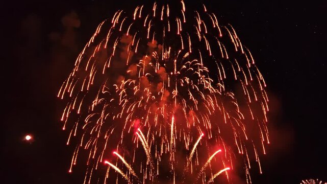 Vibrant red fireworks explode spectacularly against dark night sky