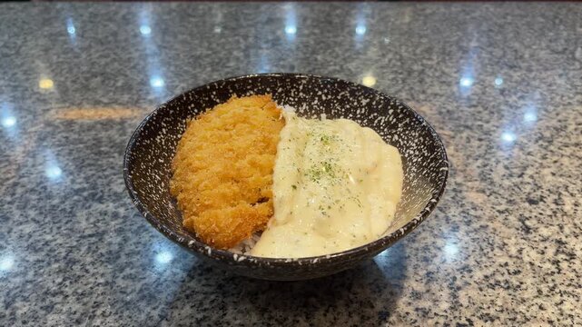 Close up view of Hokkaido Dori Donburi isolated on ceramic table. light, lights. bright. lamp, lamps. white. black and white bowl. Rice with dory fish topped with processed protein. japan, japanese.