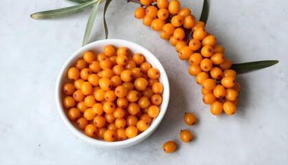 Fototapeta premium Freshly picked bright orange sea buckthorn berries in a white bowl and on a branch
